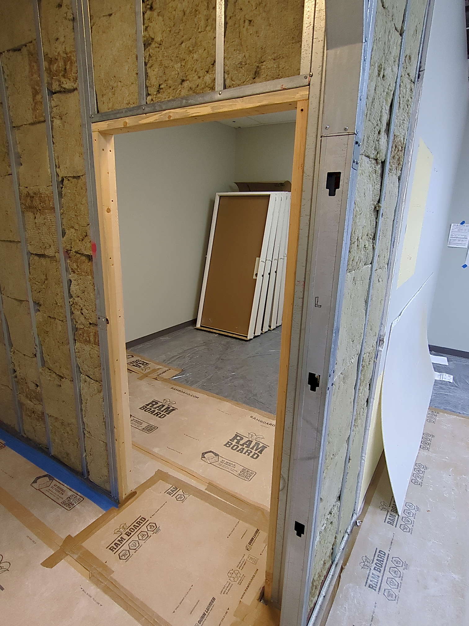 SDG pre-construction 5 The new wall in progress, all metal bones and insulation. Inside the room, several brand new doors lean against the back wall.